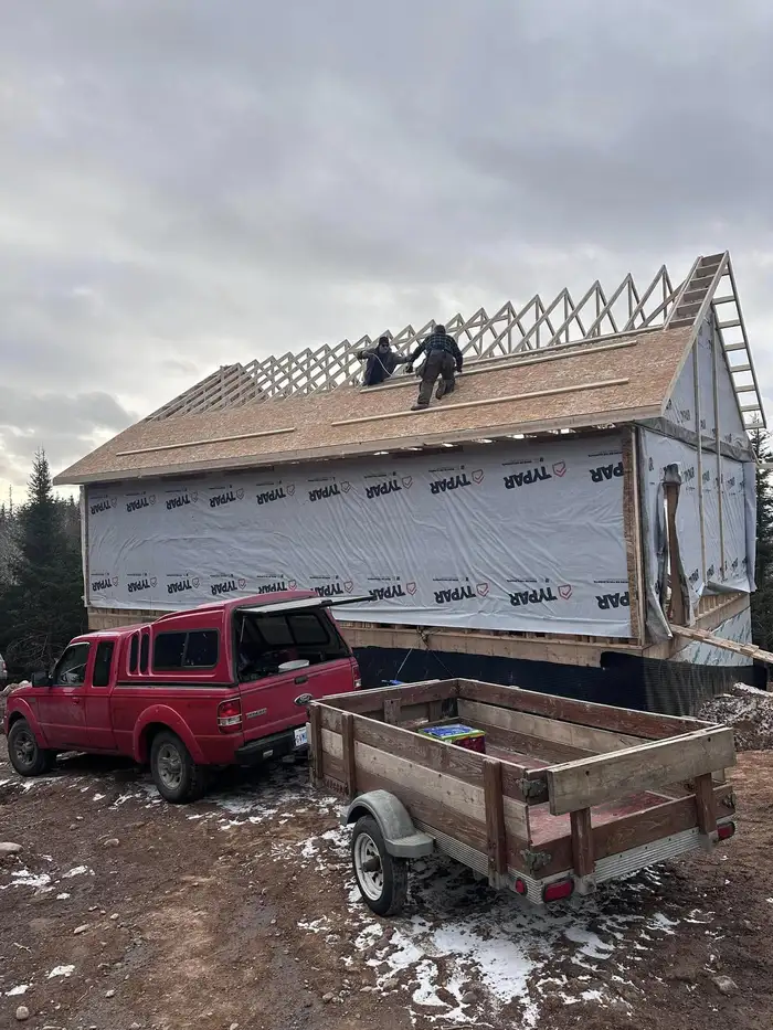 Ongoing construction of a house with workers on the roof and vehicles nearby.
