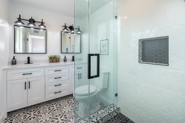 A stylish modern bathroom featuring a glass shower, white cabinetry, and patterned tiles.