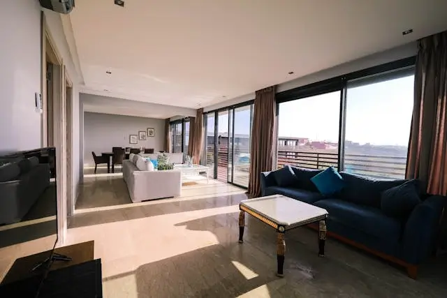 A modern living room with large windows, bright sunlight, and stylish furniture.